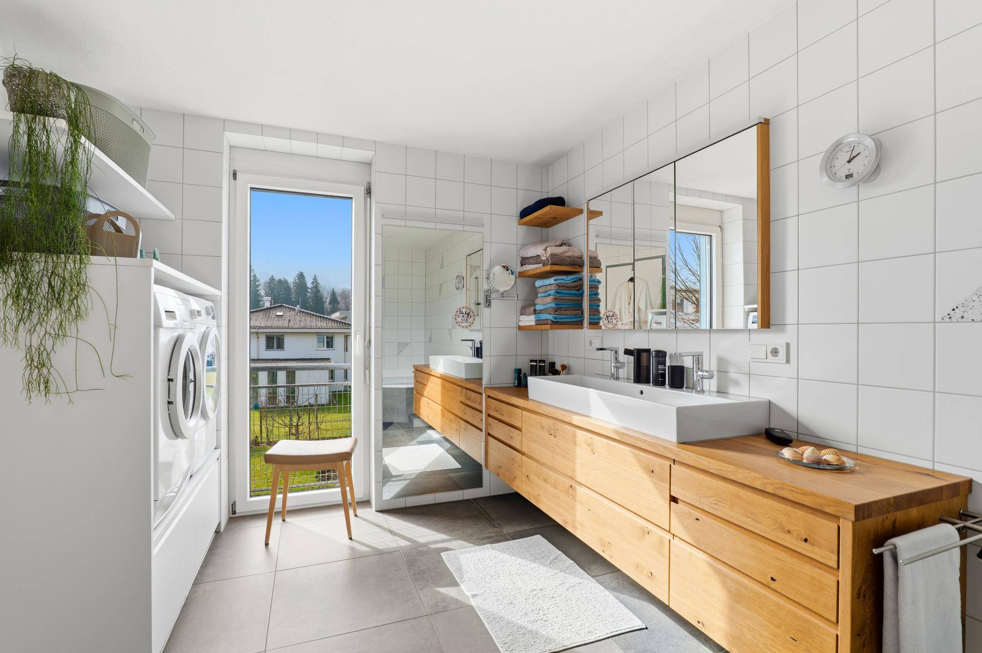 Geräumiges Badezimmer mit Doppelwaschbecken, Waschmaschine und Trockner, hell durch großes Fenster.