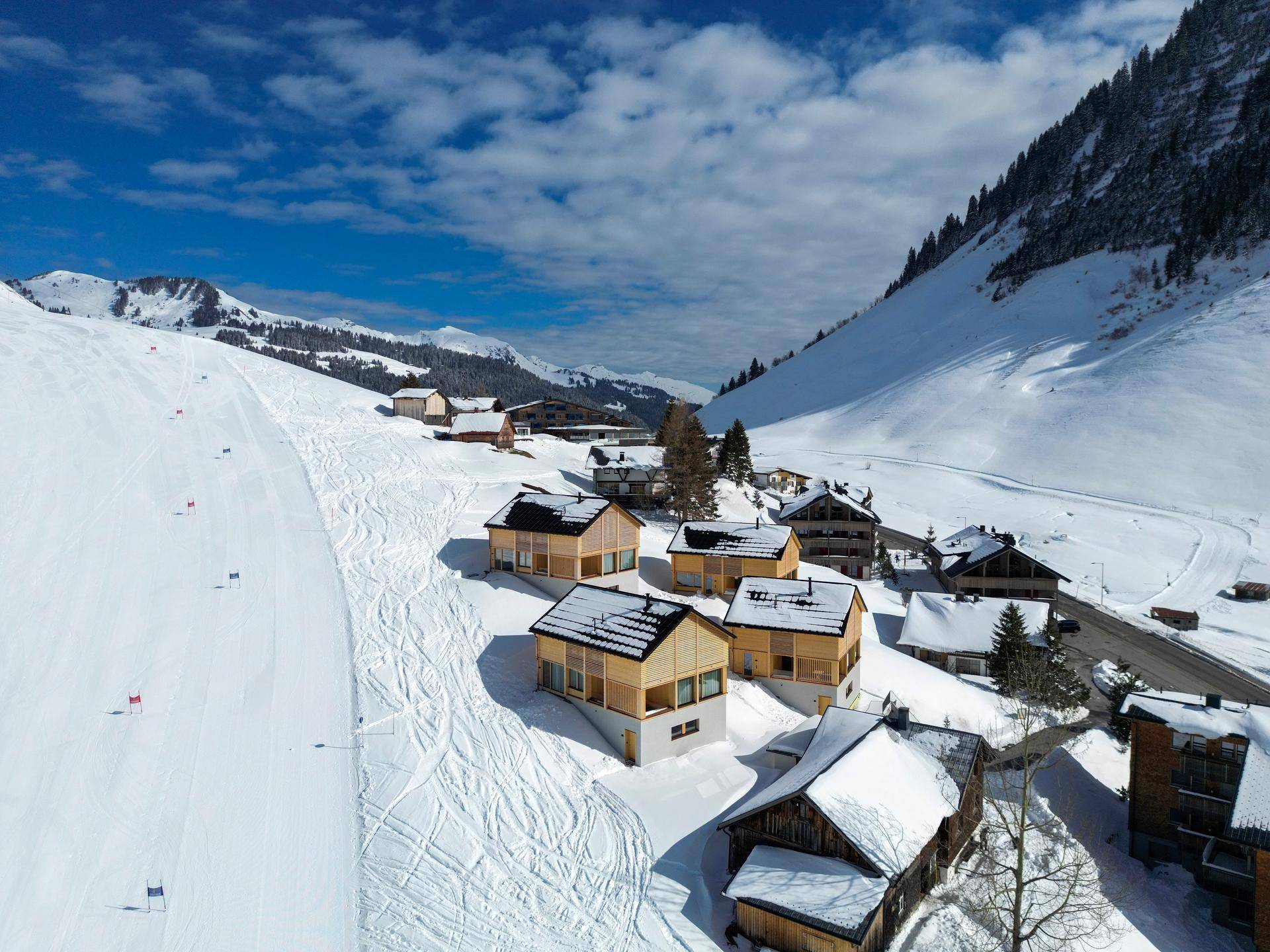 Luftaufnahme einer Gruppe von modernen Chalets in einer verschneiten Berglandschaft mit Skipisten.