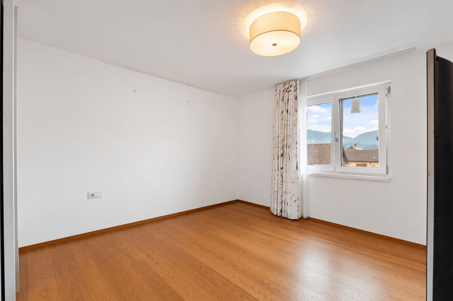 Helles Schlafzimmer mit Holzboden und Fenster, das einen weiten Blick auf die umliegende Berglandschaft bietet.