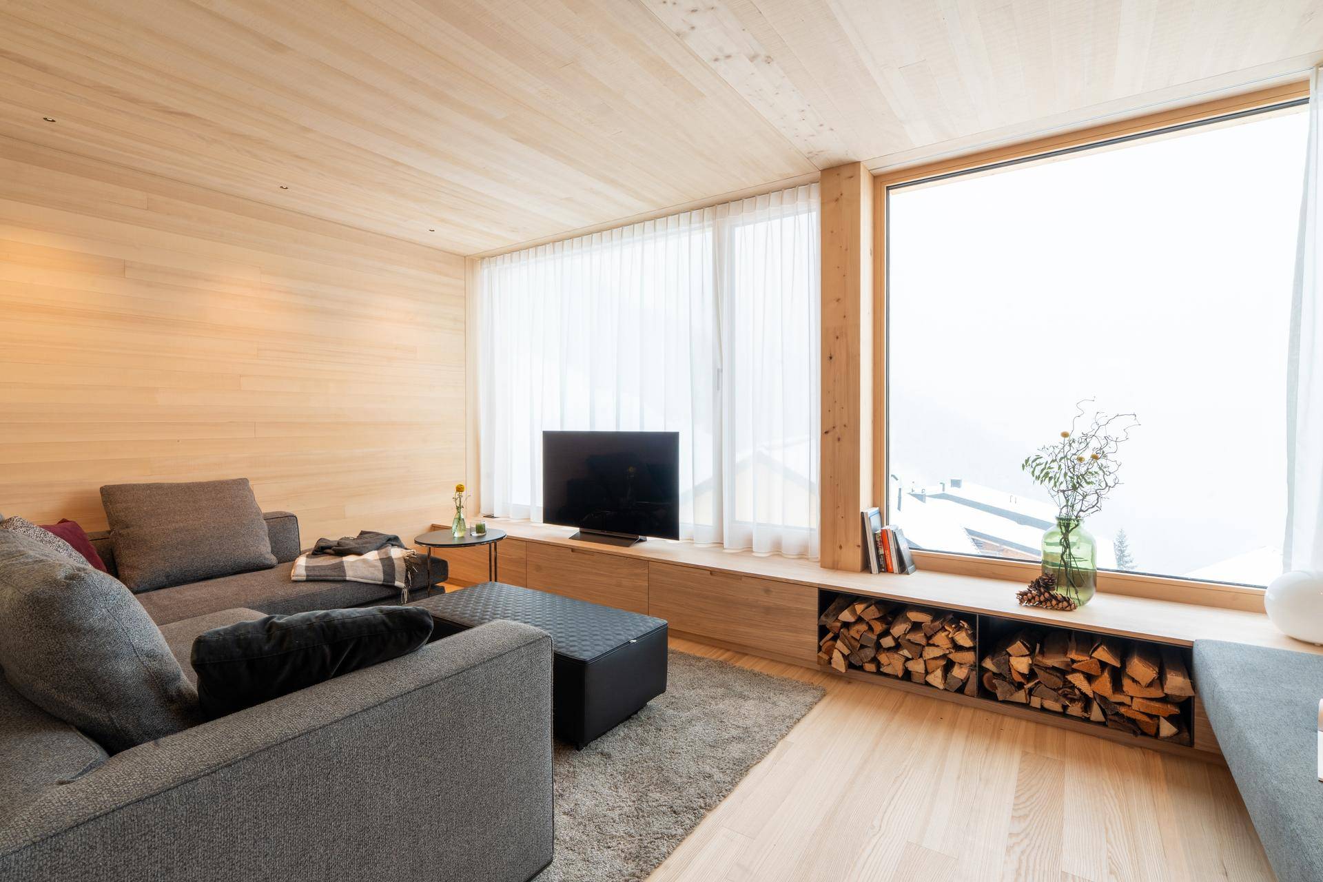 Gemütliches Wohnzimmer mit großem Sofa, Fernseher und Holzregalen für Kaminholz.