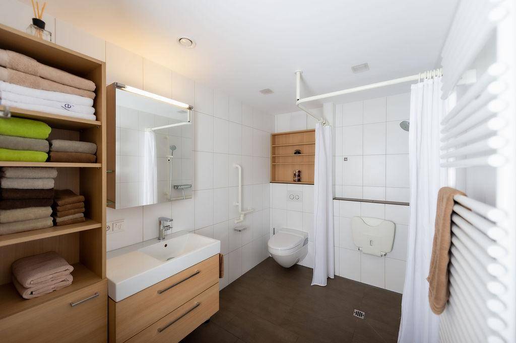 Barrierefreies Badezimmer mit Haltegriffen, wandhängendem WC und begehbarer Dusche.