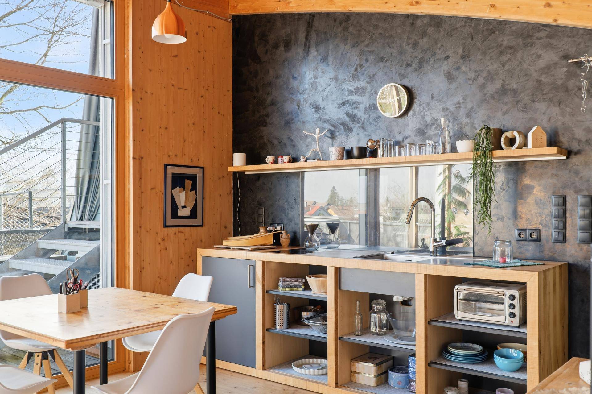 Moderne Küche mit Holzelementen, dunkler Akzentwand und Essbereich, offen zum Wohnraum.