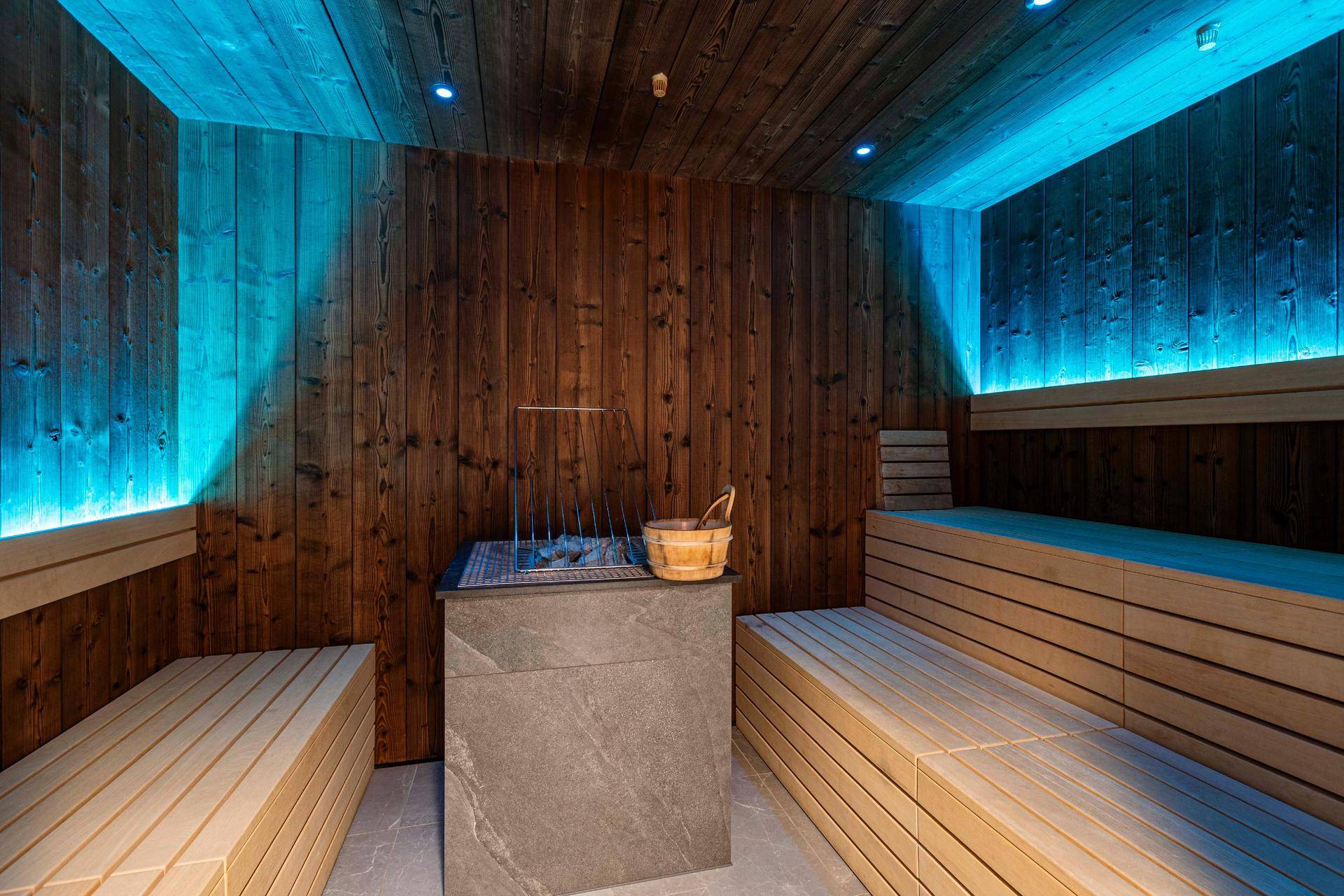 Holzvertäfelte Sauna mit Bänken und stimmungsvoller blauer Beleuchtung.