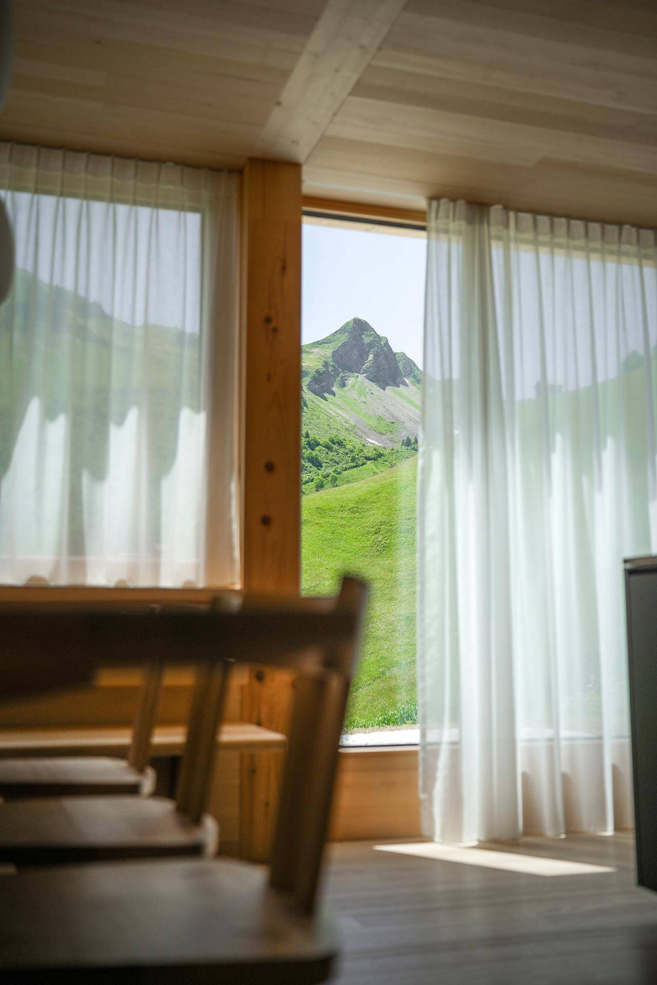 Heller Essbereich mit Holztisch und Stühlen, großen Fenstern und Blick auf die grüne Berglandschaft.