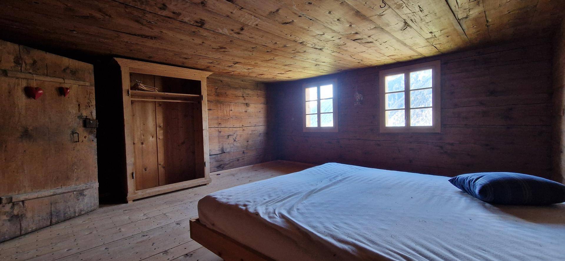 Gemütliches Schlafzimmer mit rustikalen Holzvertäfelungen, Holzboden und einem einfachen Bett.