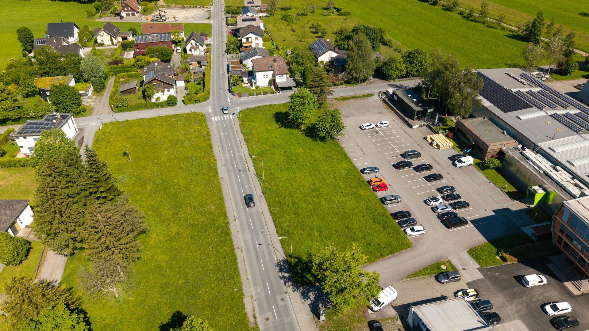 Luftaufnahme eines Grundstücks mit angrenzenden Wohngebäuden, Straßen und einem Gewerbegebiet im Hintergrund.