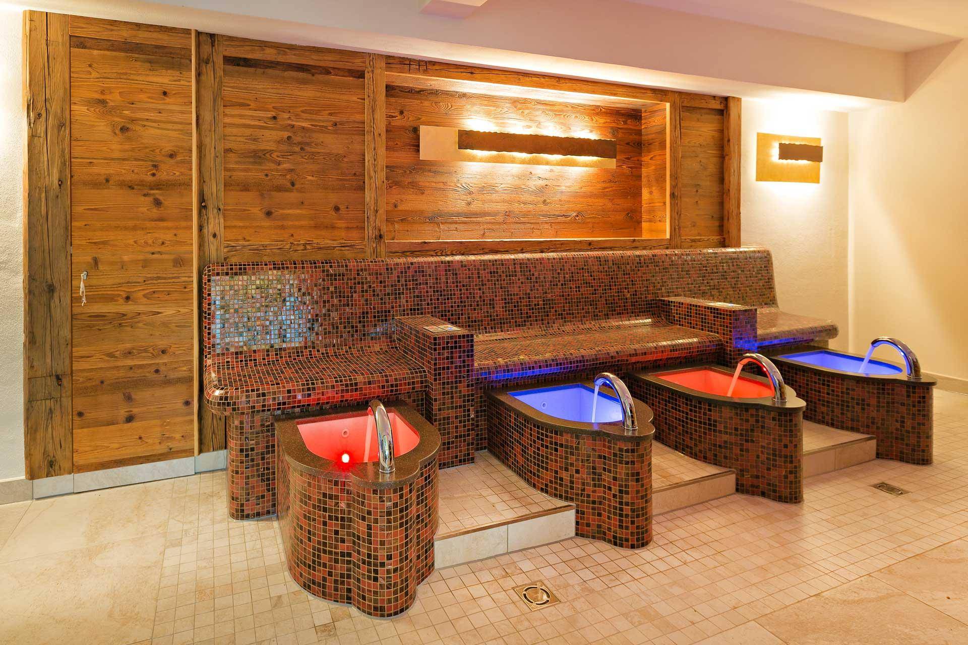 Fußbadbereich im Wellnessbereich mit Mosaikfliesen, Holzwänden und farbiger Beleuchtung.