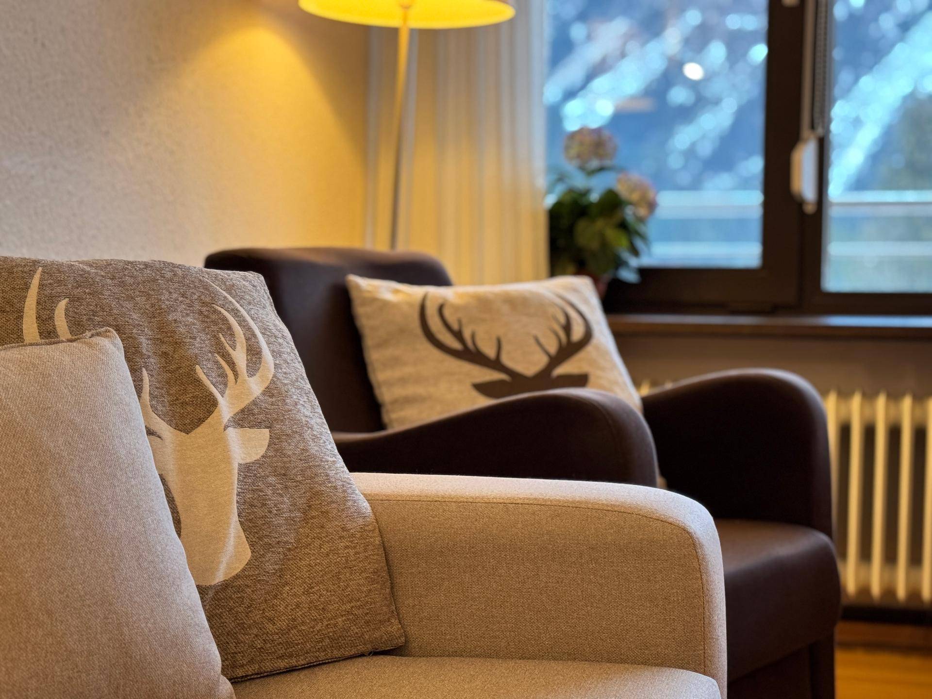 Gemütliches Sofa mit Hirschgeweih-Kissen und einer Stehlampe, mit Blick auf die Berge.