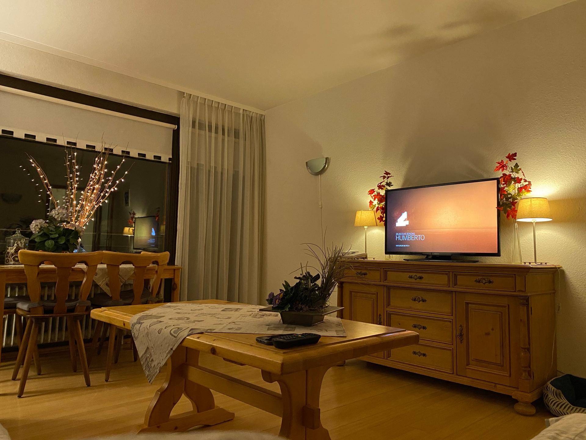 Gemütlicher Wohn-Essbereich am Abend mit Fernseher, Holztisch und stimmungsvoller Beleuchtung.