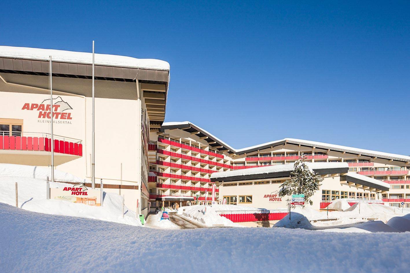 Das Aparthotel im Winter, umgeben von tiefem Schnee und klarem blauen Himmel.