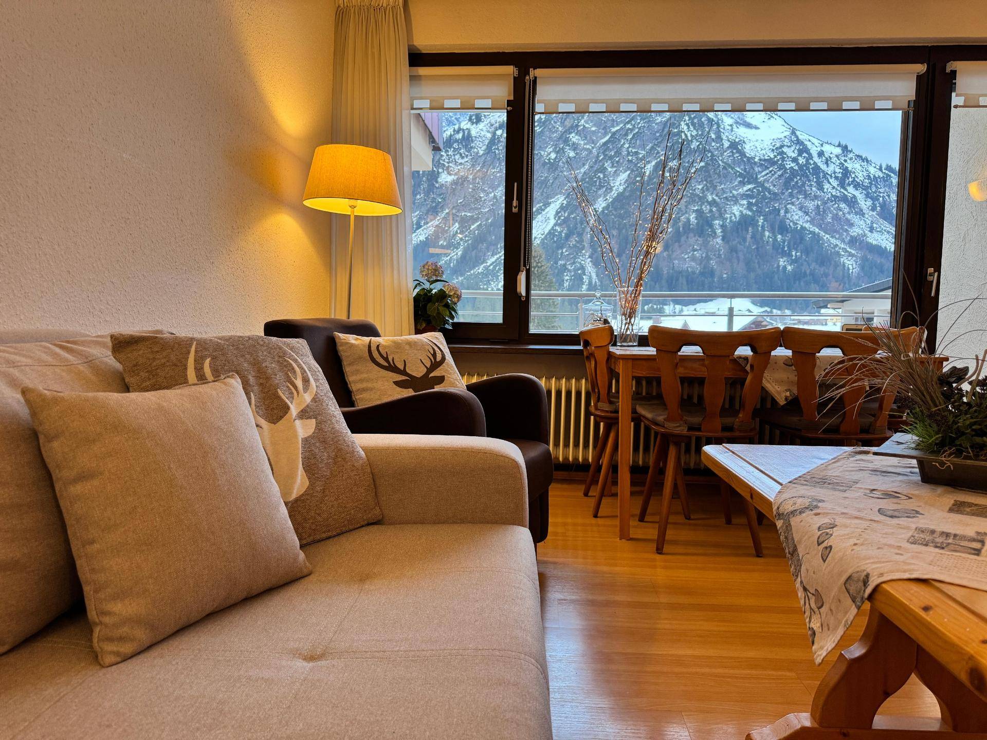 Wohn- und Essbereich mit Sofa, Esstisch und großem Fenster mit Blick auf schneebedeckte Berge.