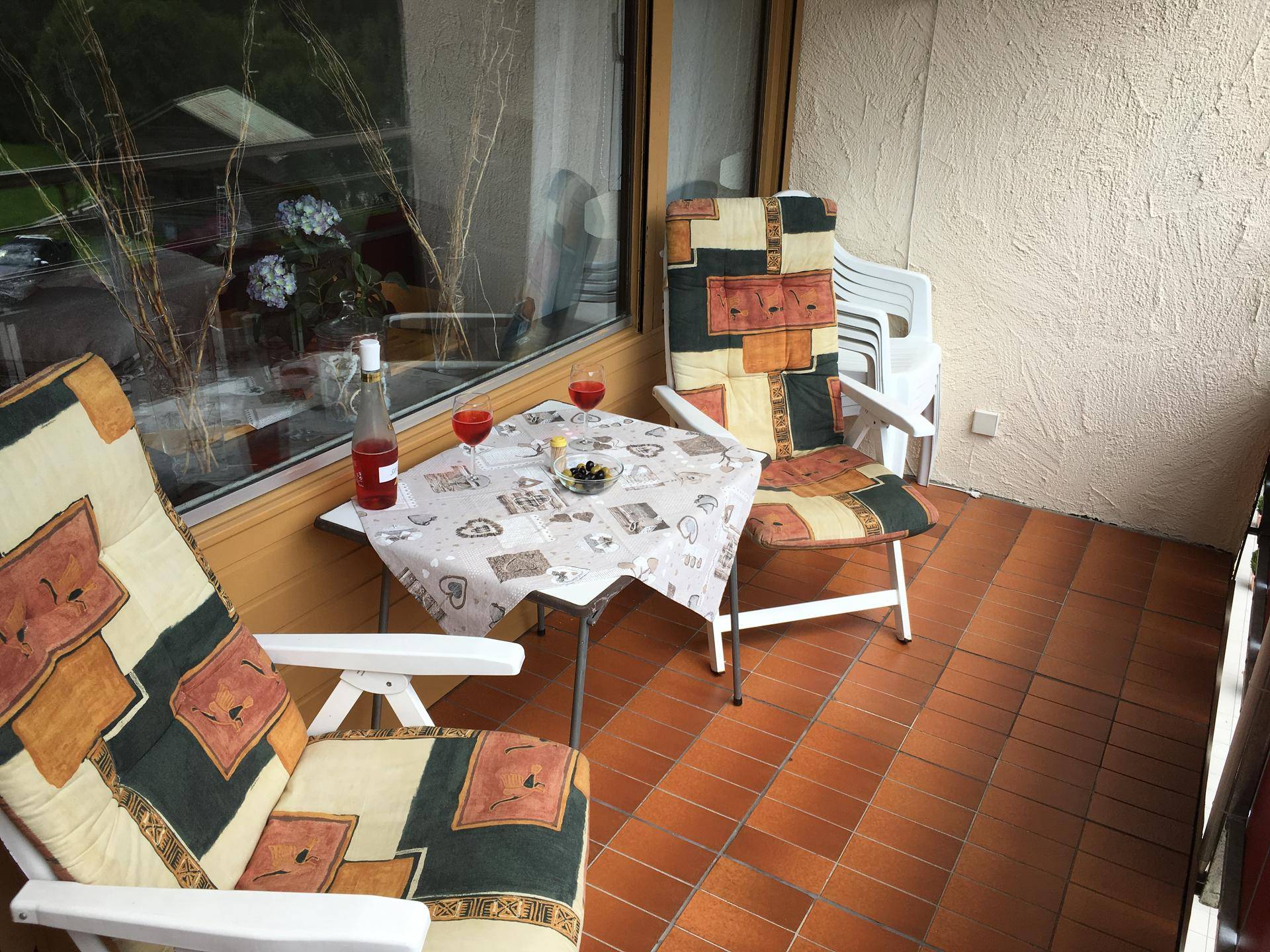 Kleiner Balkon mit Terrakottafliesen, Tisch und Stühlen, ideal für entspannte Stunden im Freien.