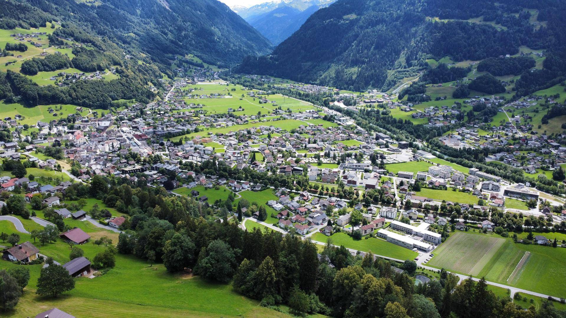 Weitläufige Luftaufnahme einer Stadt in einem Tal, umgeben von Bergen und grünen Feldern.