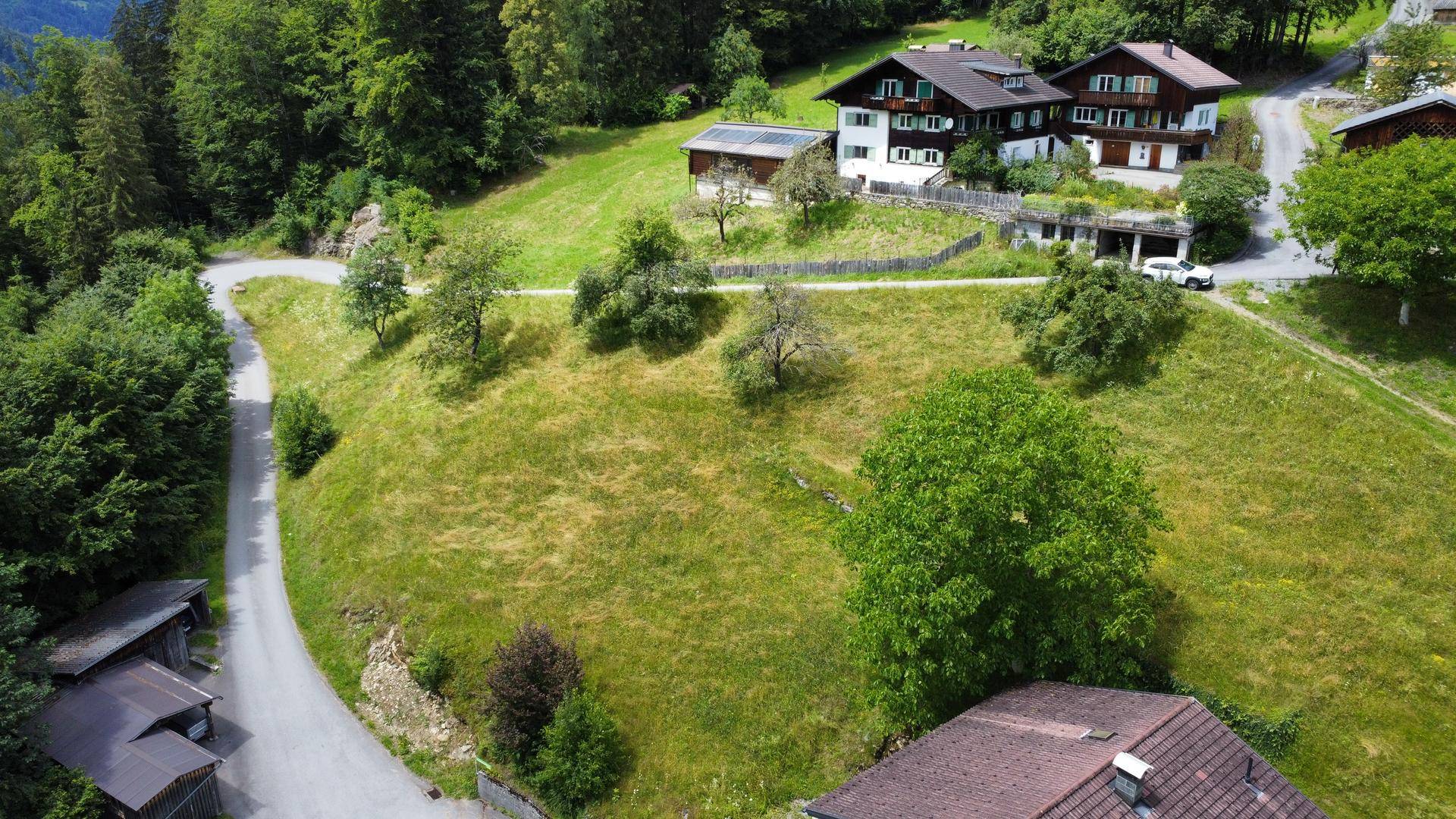 Luftaufnahme einer hügeligen Landschaft mit mehreren Häusern und kurvigen Straßen.