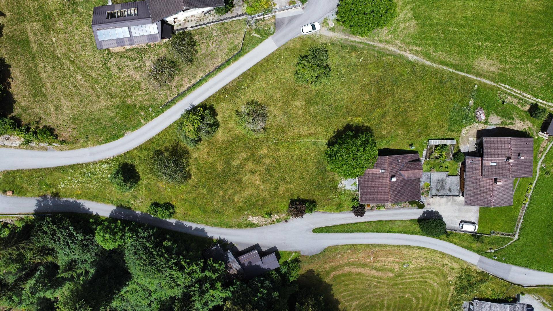 Vogelperspektive auf Wohnhäuser, Straßen und grüne Grundstücke in ländlicher Umgebung.
