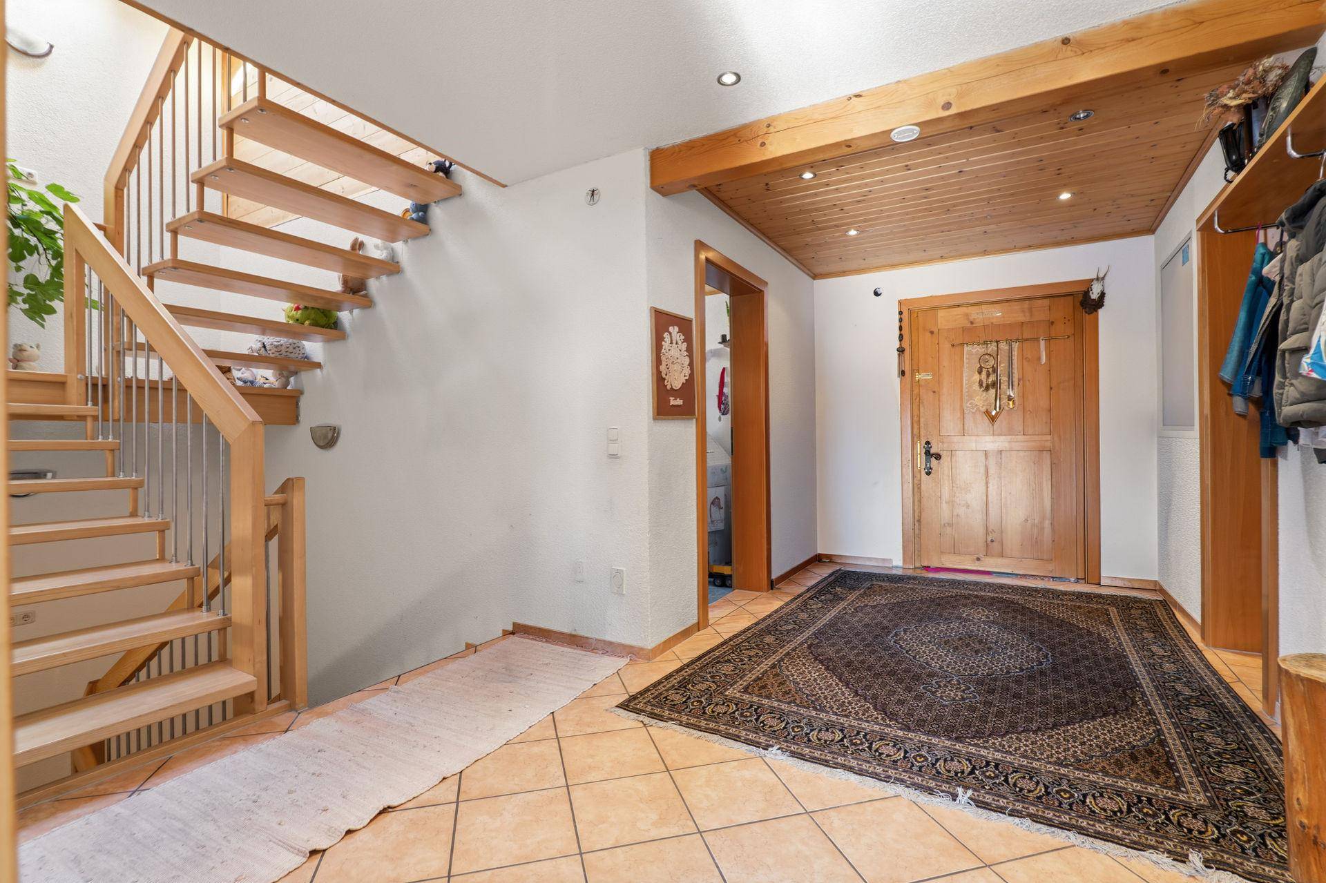 Heller Eingangsbereich mit Holztreppe, Fliesenboden und traditioneller Holztür.