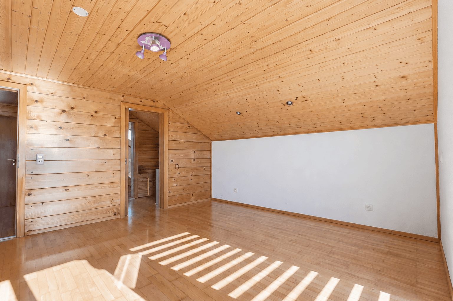 Helles Schlafzimmer im Dachgeschoss mit Holzverkleidung, Holzboden und viel Tageslicht.