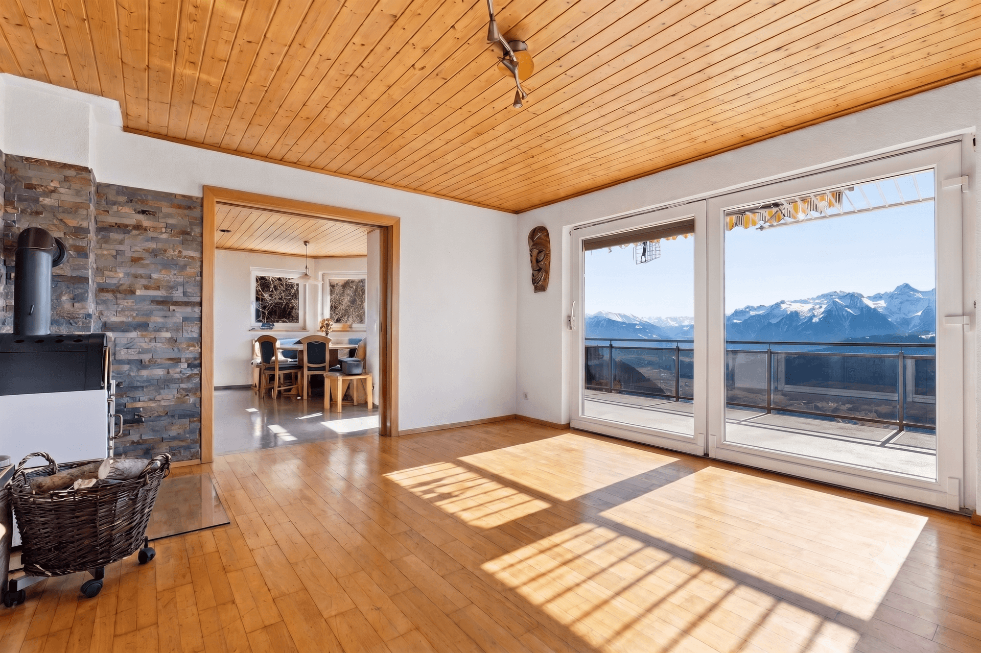 Gemütliches Wohnzimmer mit Holzboden, Kaminofen und Zugang zu einem Balkon mit Bergblick.