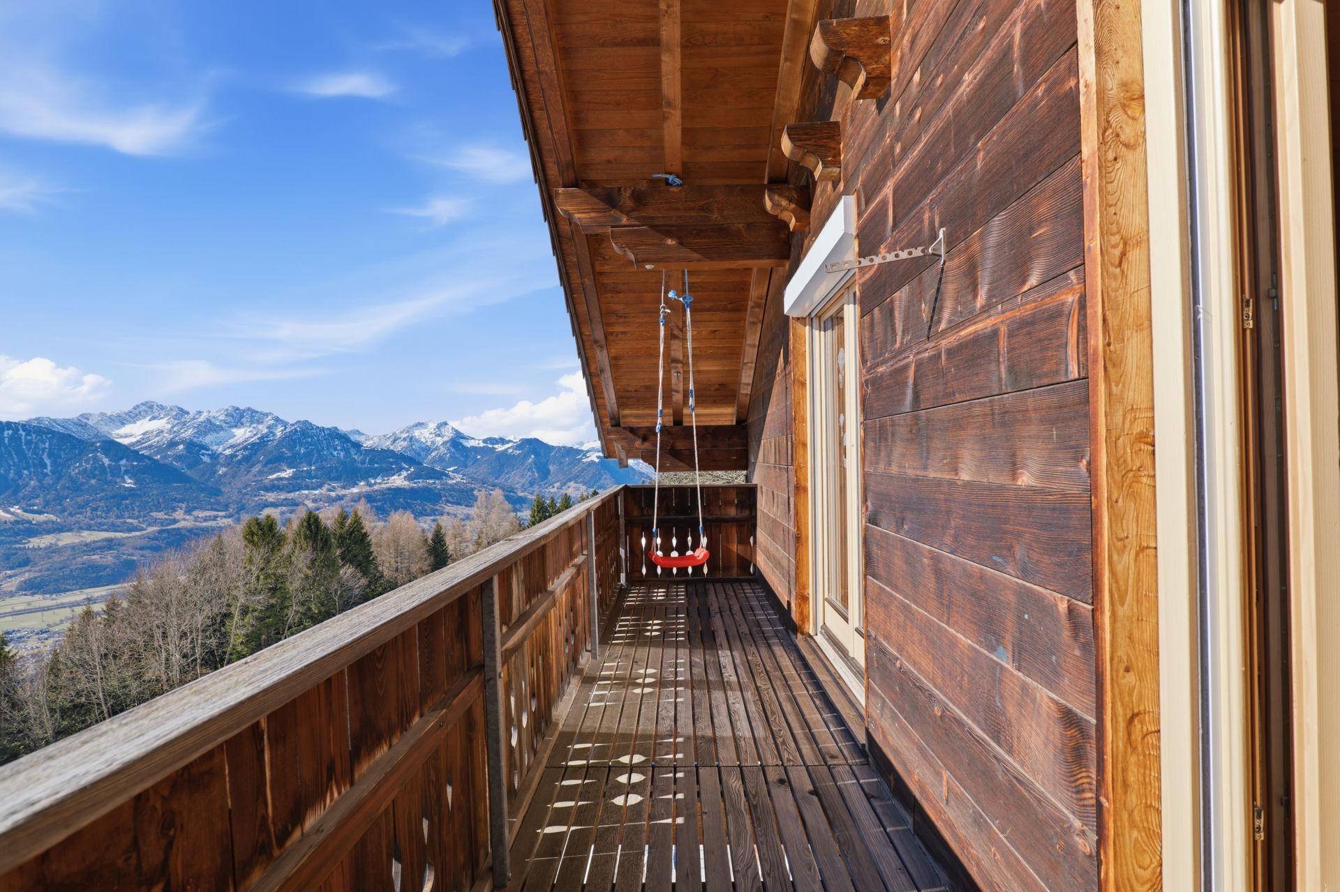 Langer Holzbalkon mit Schaukel und weitem Blick auf die umliegende Berglandschaft.