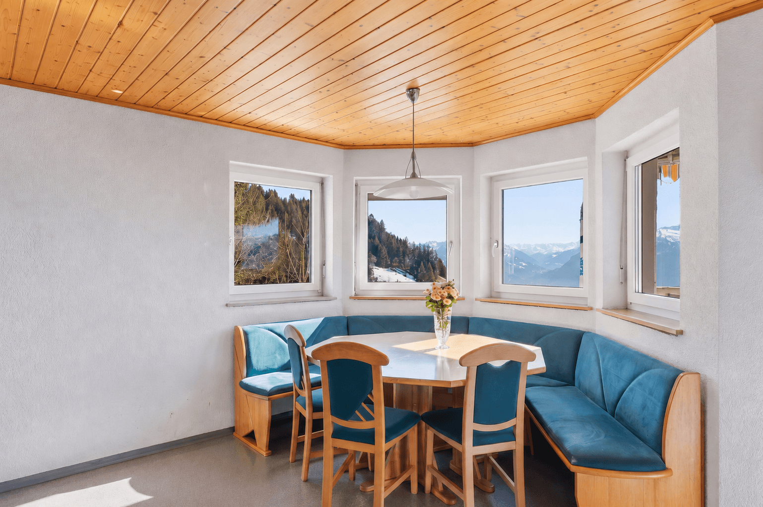Heller Essbereich mit Holztisch, blauen Sitzbänken und Panoramablick auf die Berge.