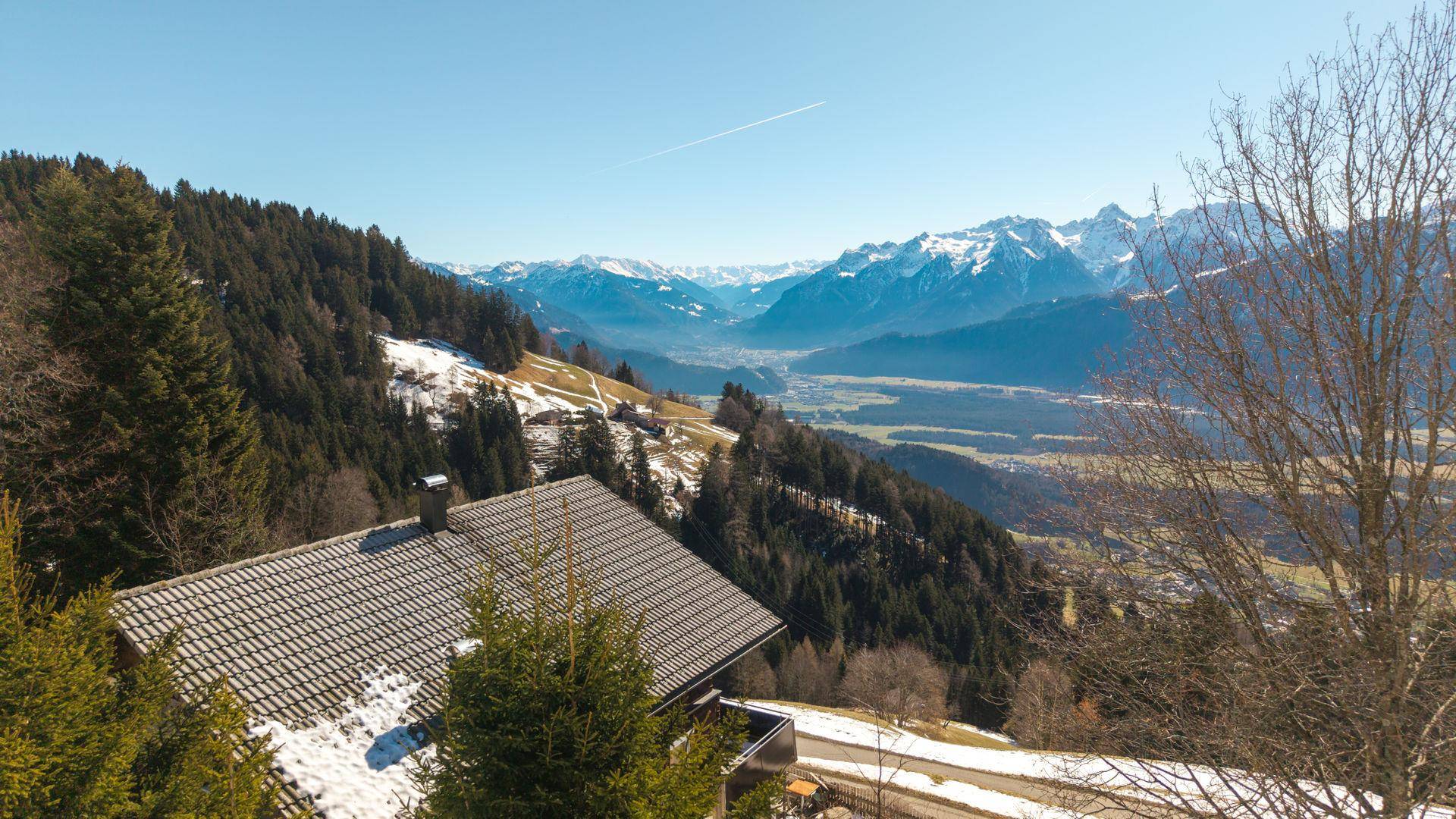 Malerische Berglandschaft mit einem Haus im Vordergrund unter blauem Himmel.
