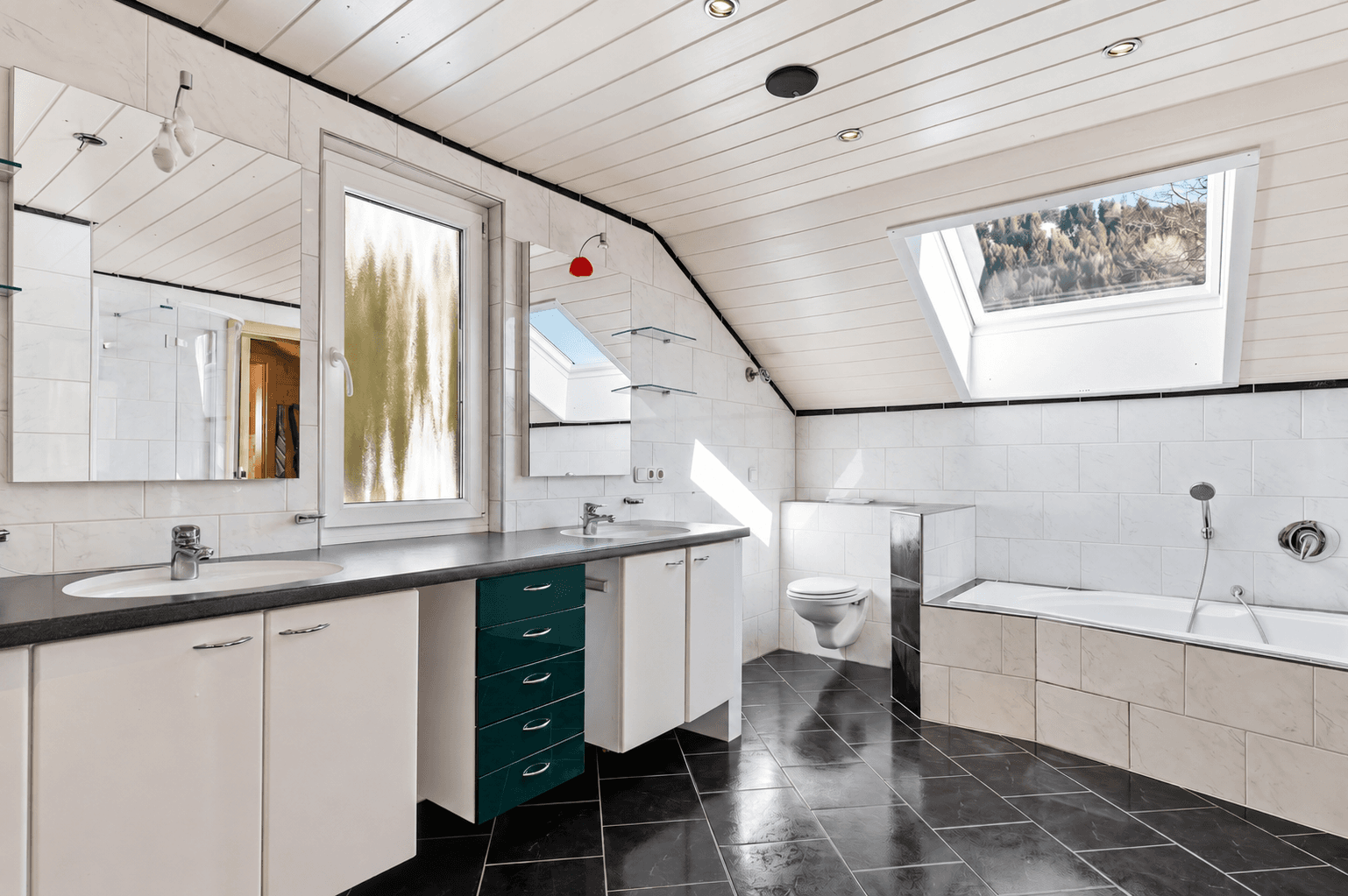 Helles Badezimmer mit Badewanne, WC, Doppelwaschbecken und Dachfenster für Tageslicht.