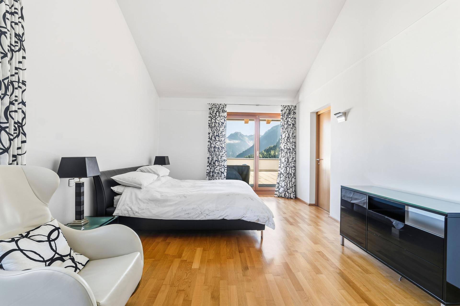 Schlafzimmer mit Zugang zum Balkon, Bergblick und hellem Holzboden.