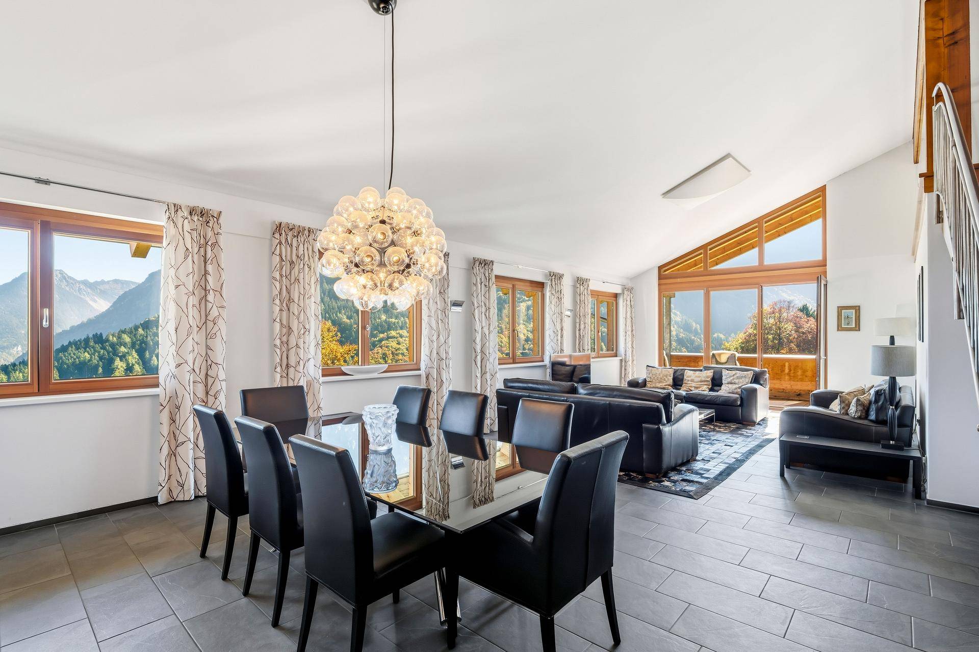 Heller Wohn-Essbereich mit großen Fenstern, Bergblick und modernem Kronleuchter.