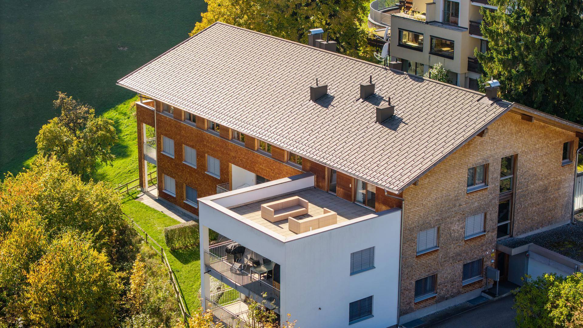Luftaufnahme des modernen Gebäudes mit Holzfassade und Terrassen in alpiner Umgebung.