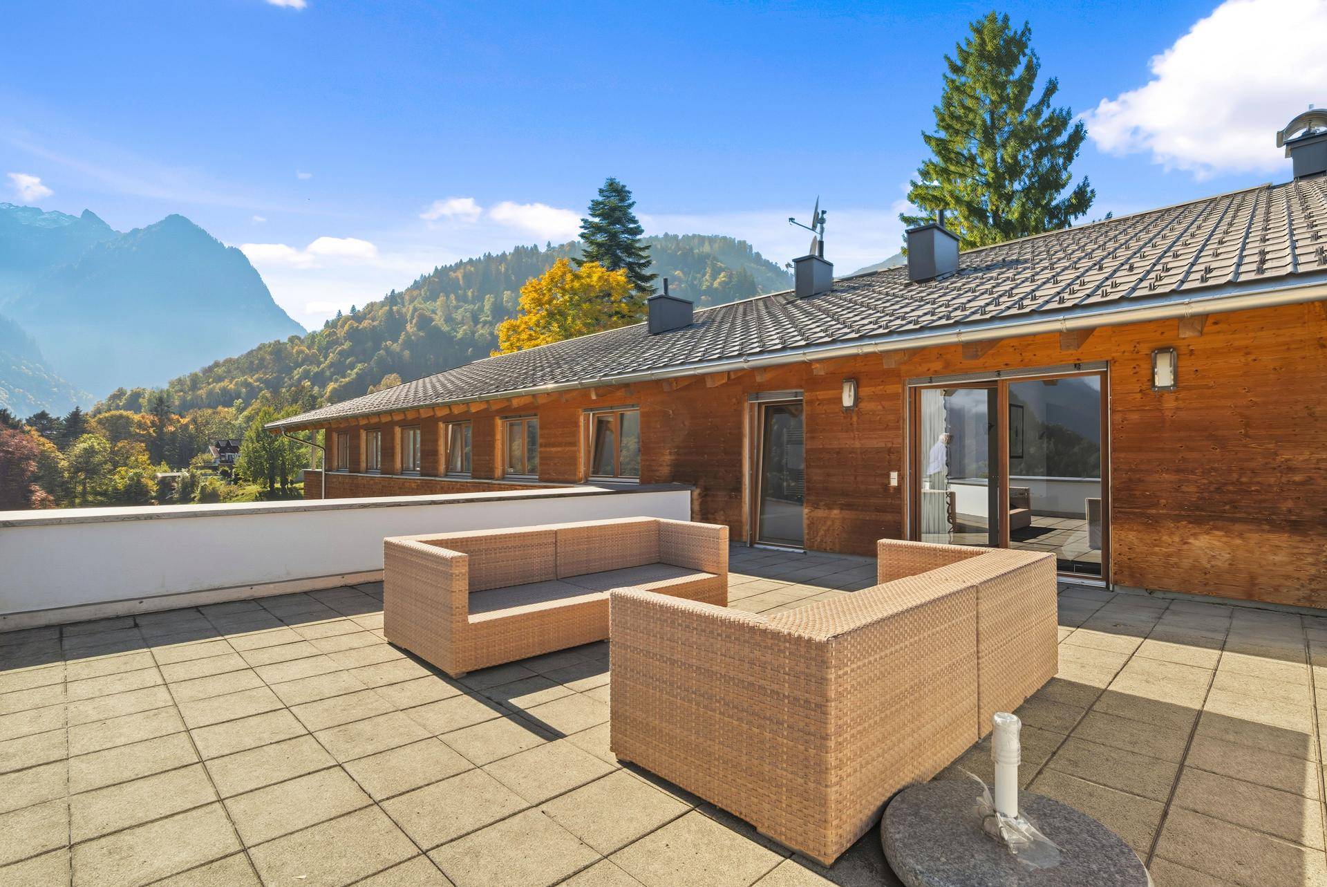 Große Terrasse mit Lounge-Möbeln vor der Holzfassade des Gebäudes und Bergblick.