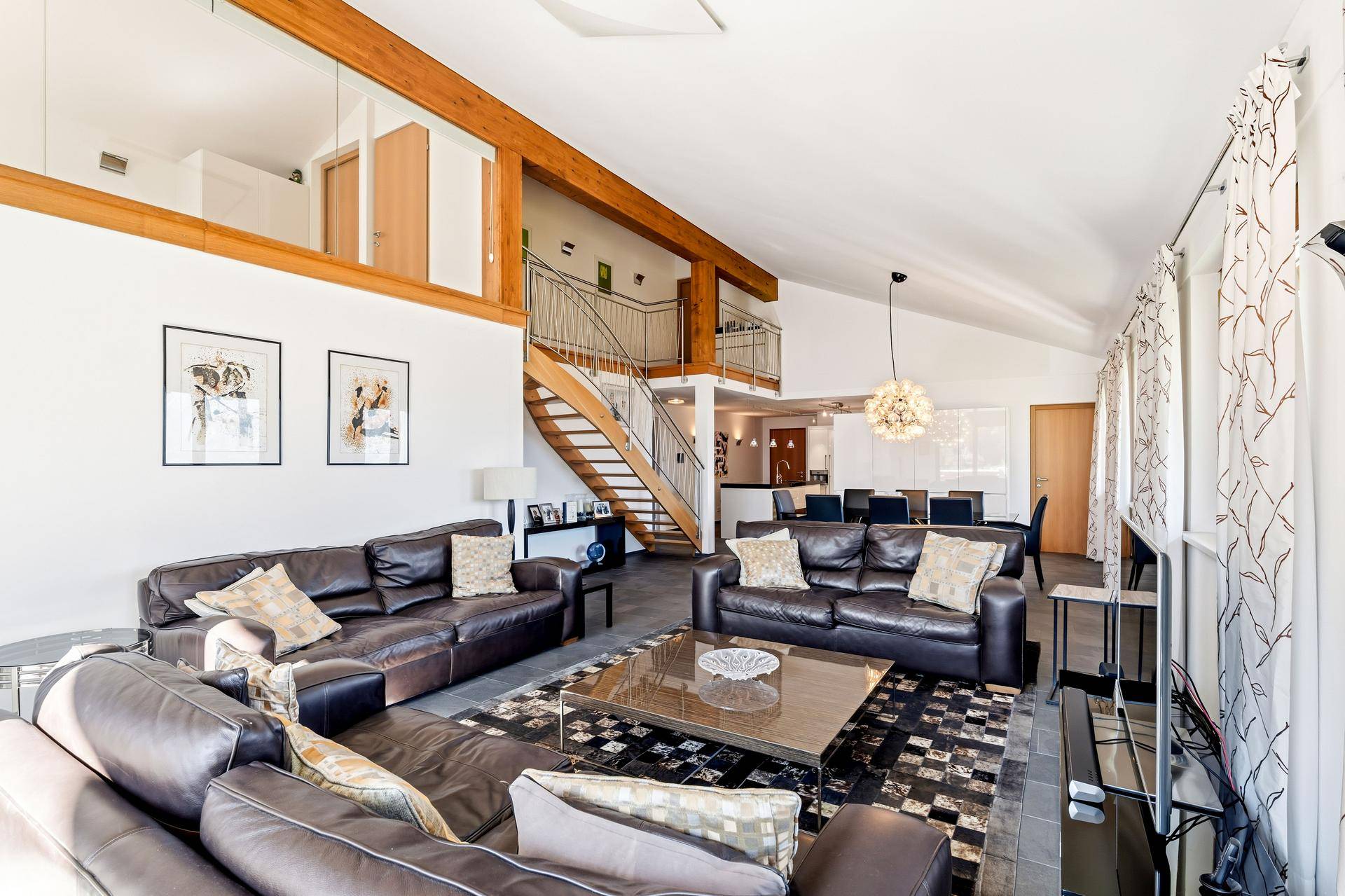 Geräumiges Wohnzimmer mit hohen Decken, Ledersofas und offener Treppe zum Obergeschoss.