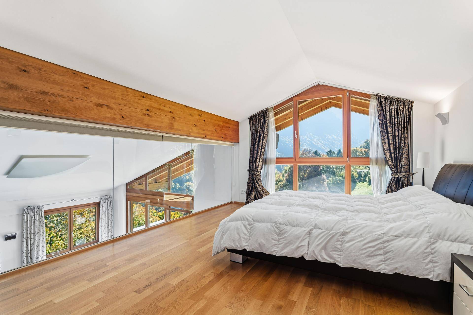 Schlafzimmer mit großen Panoramafenstern, Bergblick und Holzbalken an der Decke.