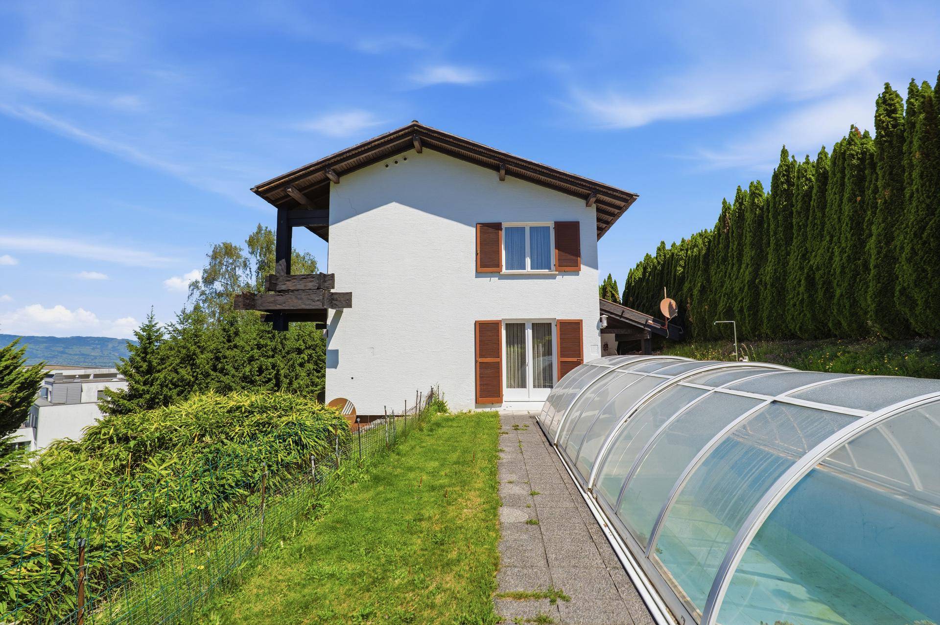 Seitenansicht des Hauses mit überdachtem Poolbereich und gepflegtem Garten.