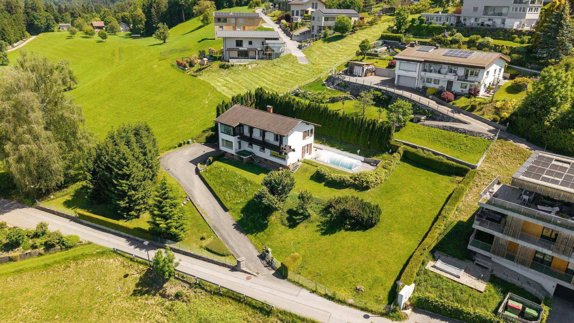 Luftaufnahme eines Anwesens mit Einfamilienhaus, Pool und weitläufigem Garten in grüner Umgebung.