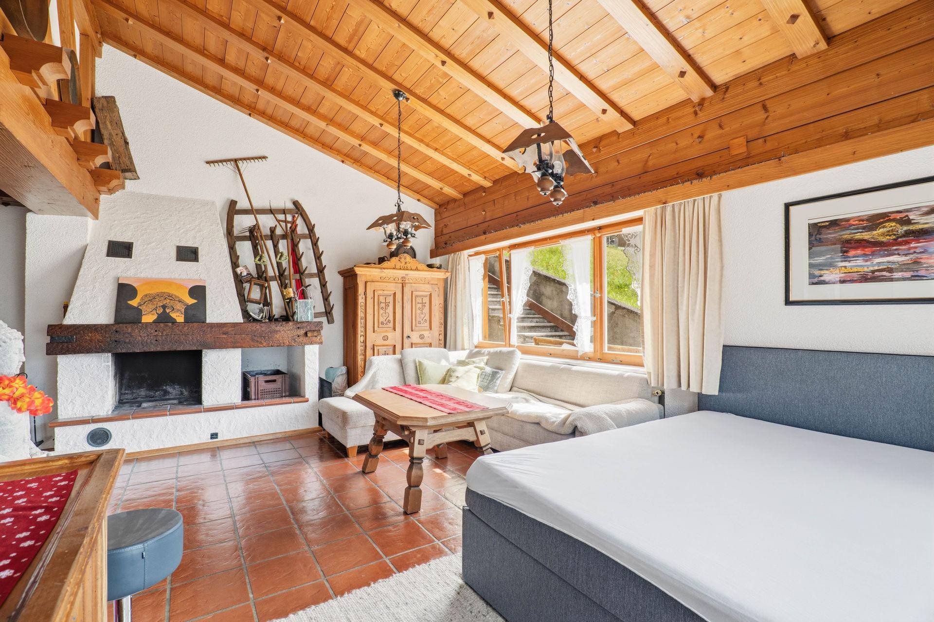 Geräumiges Wohnzimmer mit Kamin, Holzbalkendecke und Schlafgelegenheit.