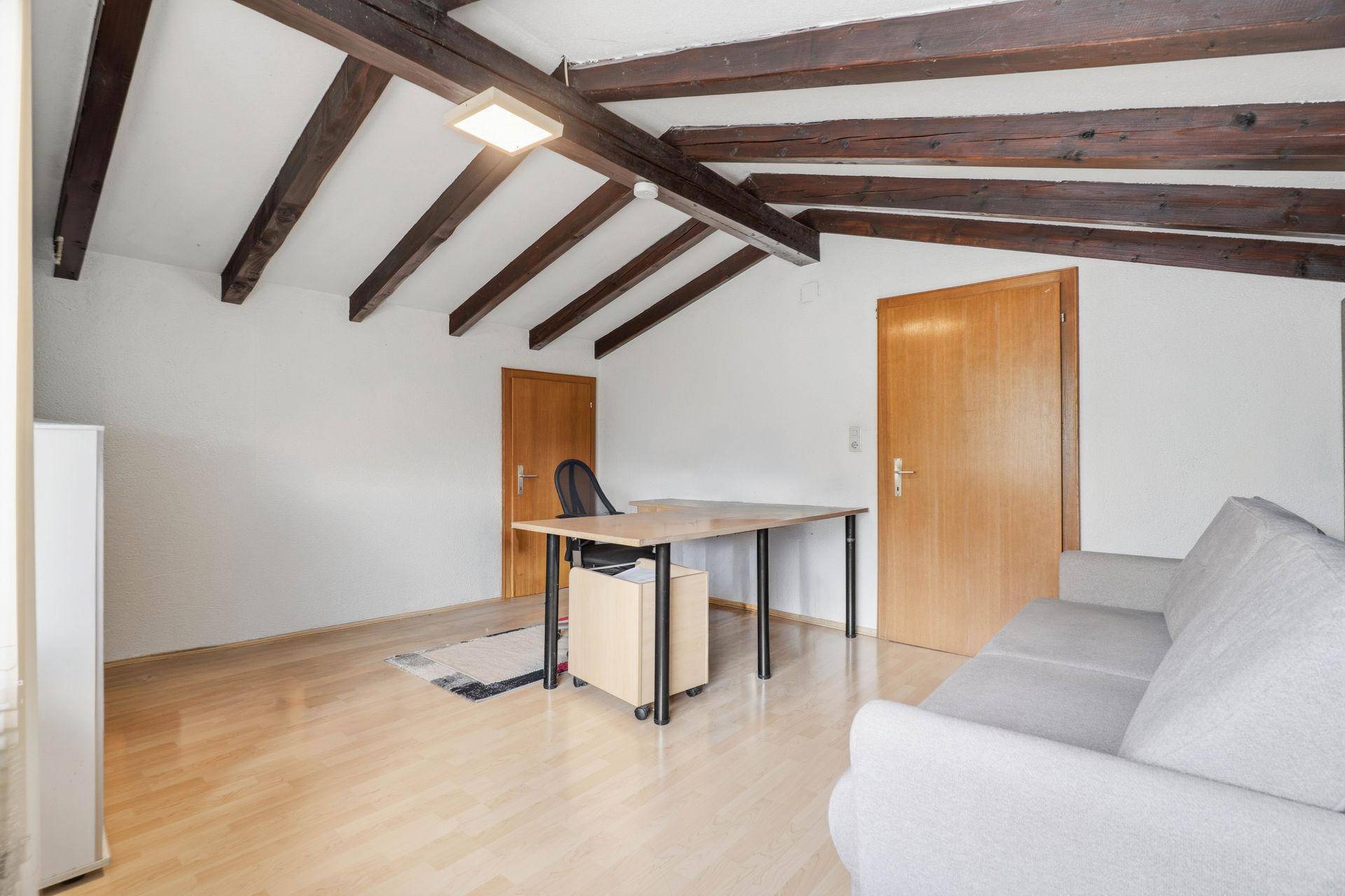 Dachgeschoss-Büro mit Holzbalken, Holzboden und Schreibtisch.