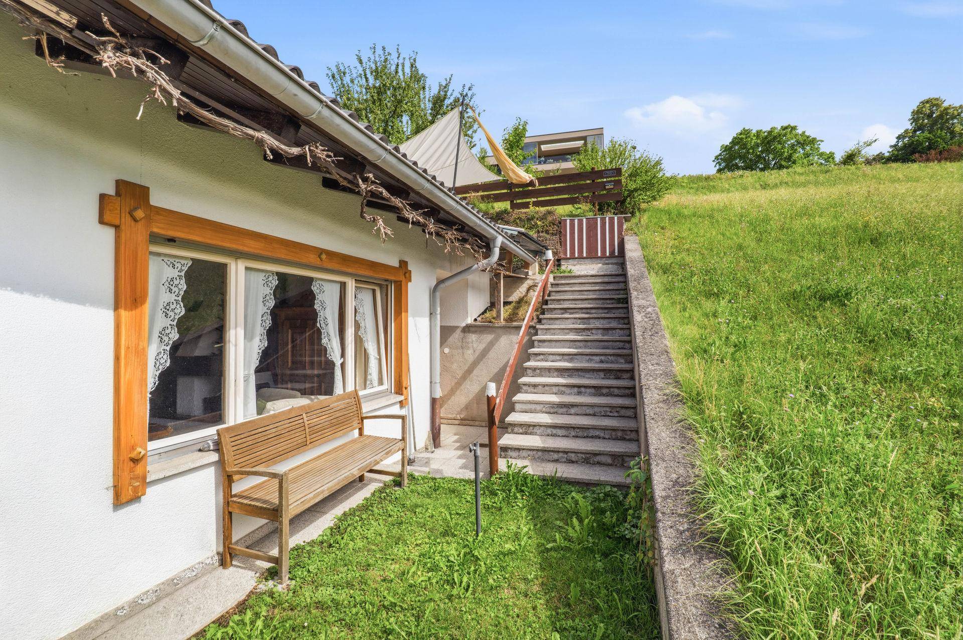 Gartenbereich mit Holzbank und Treppe, umgeben von grüner Wiese.