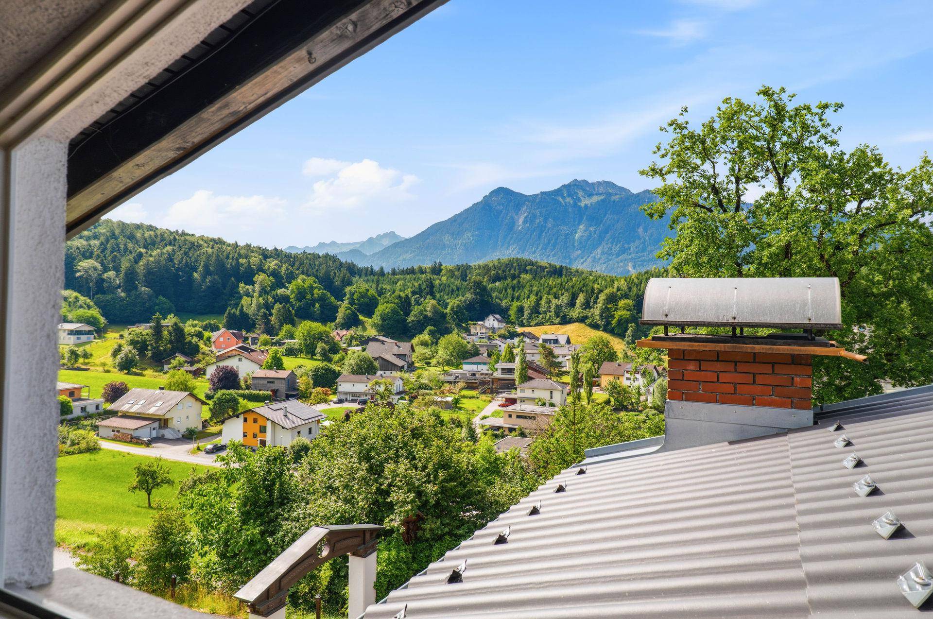 Panoramablick über ein Dorf mit Bergen und Dächern im Vordergrund.