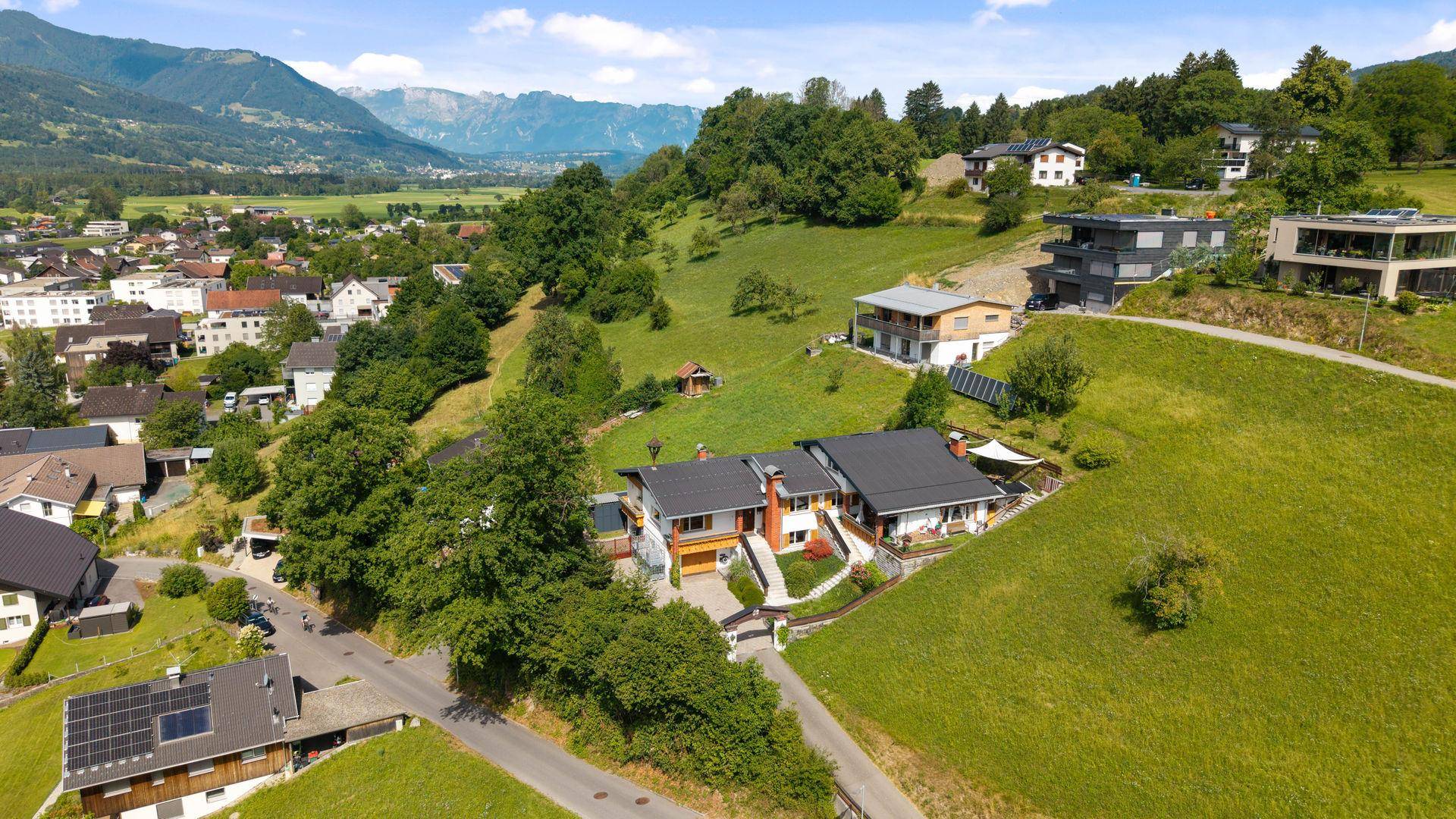 Weitläufige Luftaufnahme eines Hauses in einer grünen Hügellandschaft.