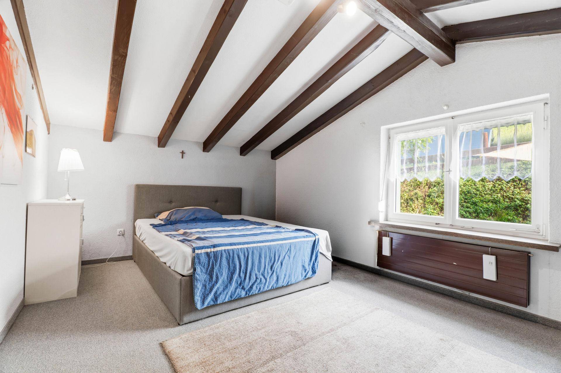 Schlafzimmer im Dachgeschoss mit Holzbalken, Teppichboden und Fenster.