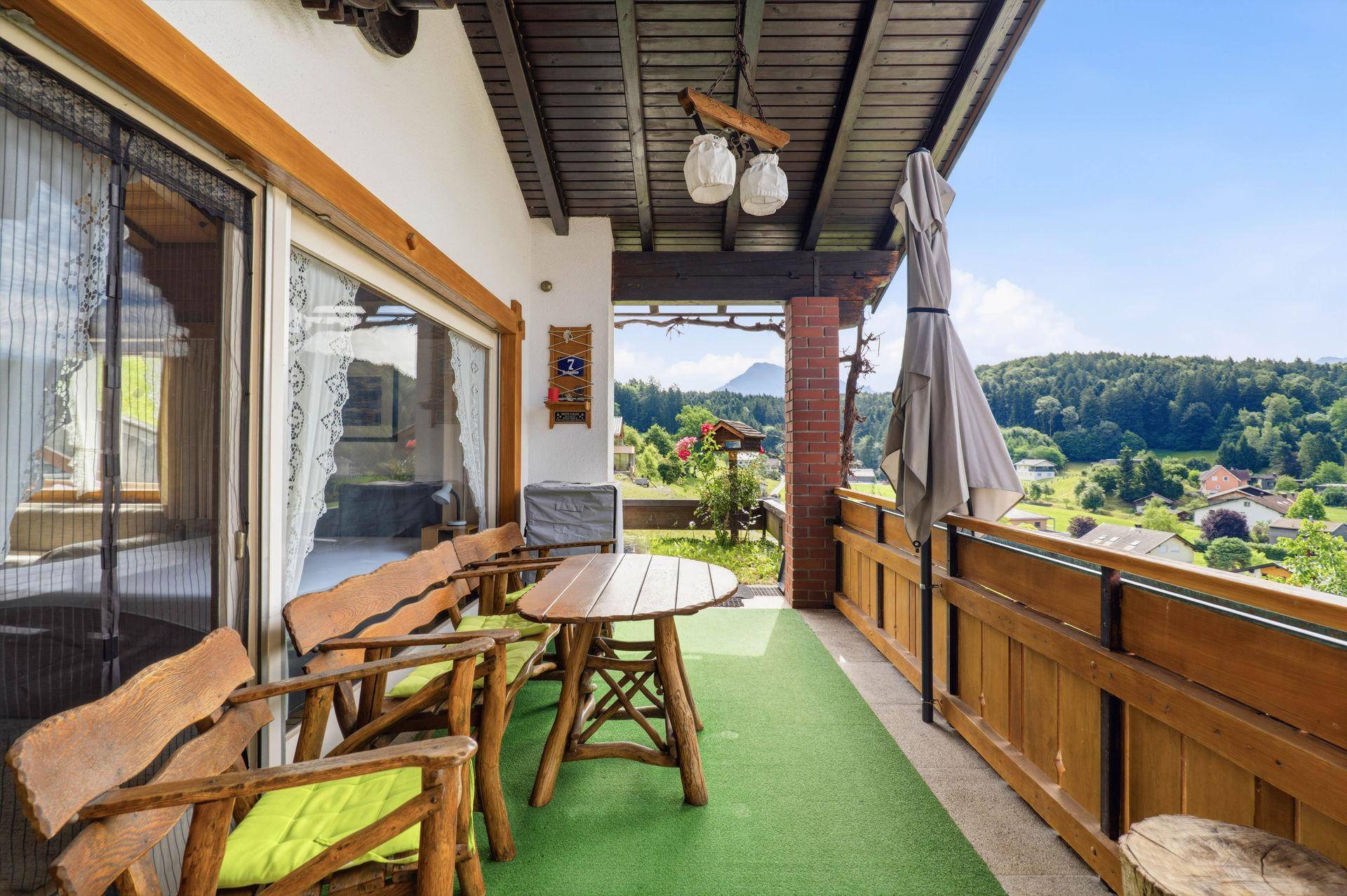 Gemütlicher Balkon mit Holzmöbeln, Bergblick und grüner Umgebung.