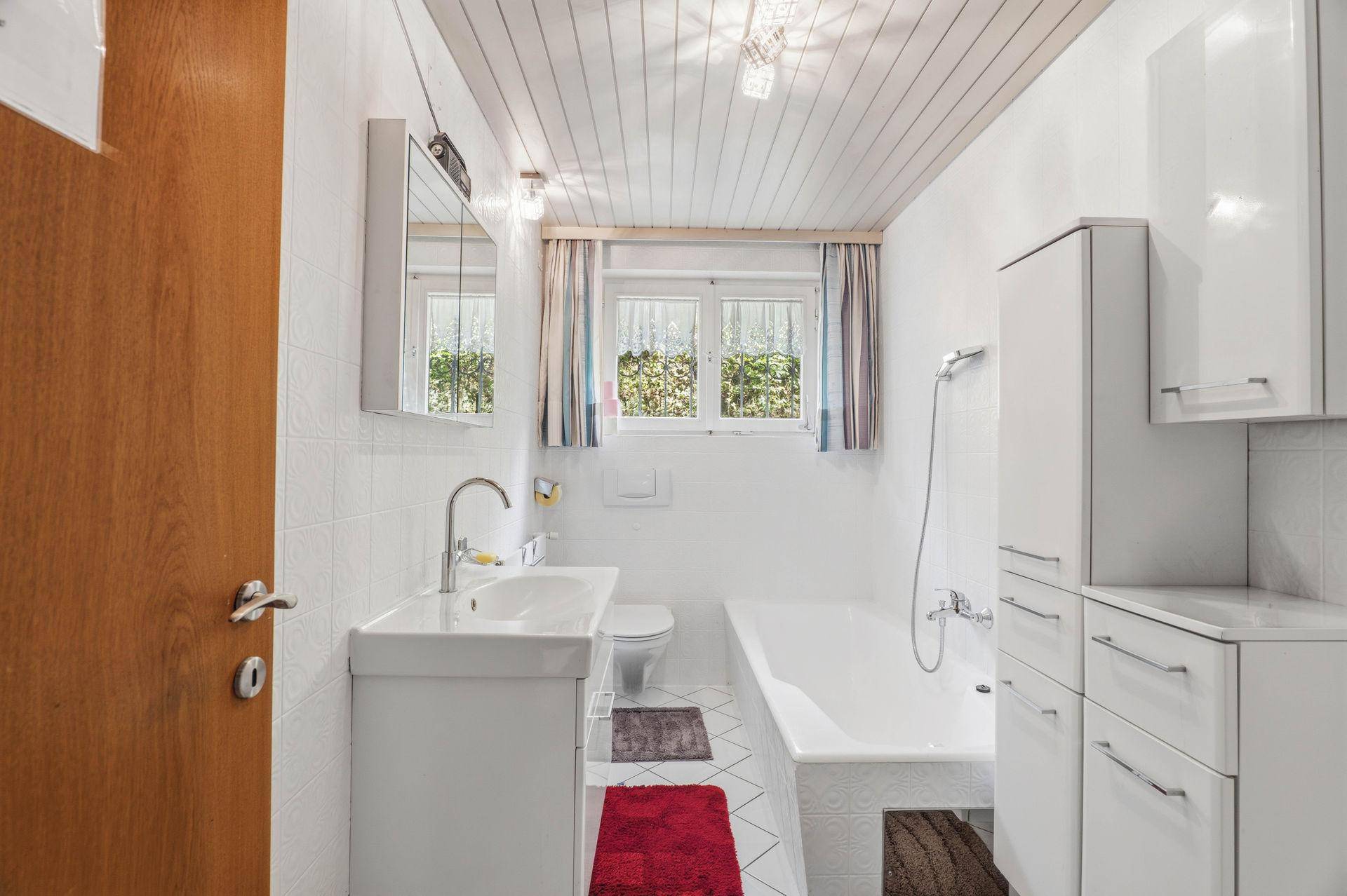 Helles Badezimmer mit Badewanne, Waschbecken und Fenster.