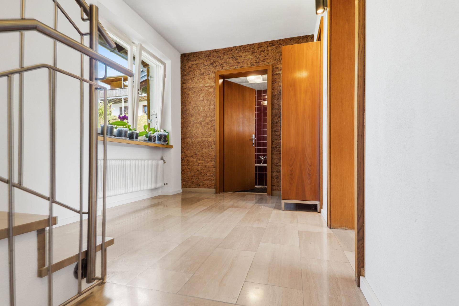 Heller Flur mit Holztreppe, Metallgeländer und Fensterbank mit Pflanzen.