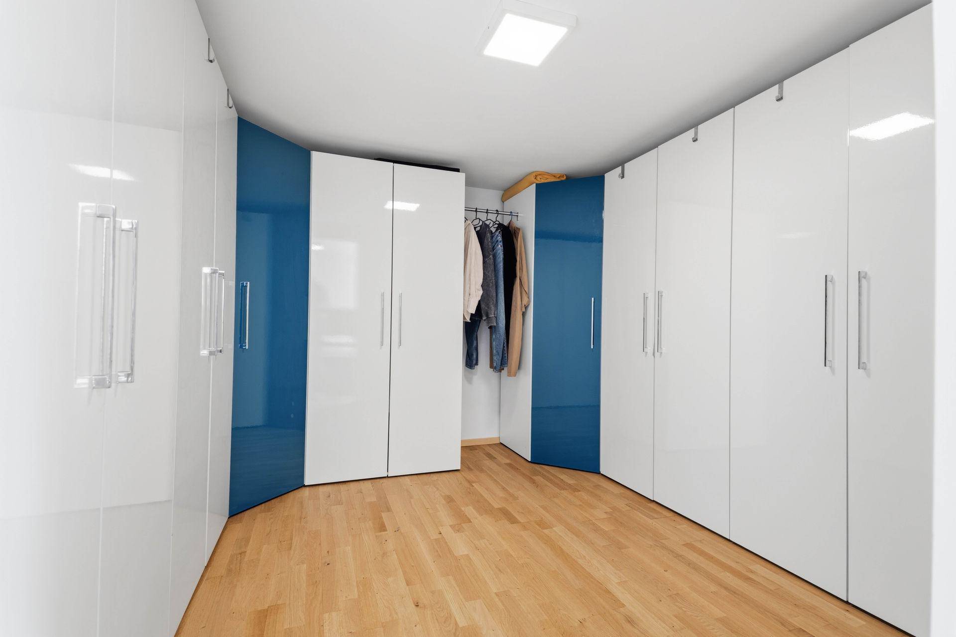 Geräumiger begehbarer Kleiderschrank mit weißen und blauen Hochglanzschränken und Holzboden.