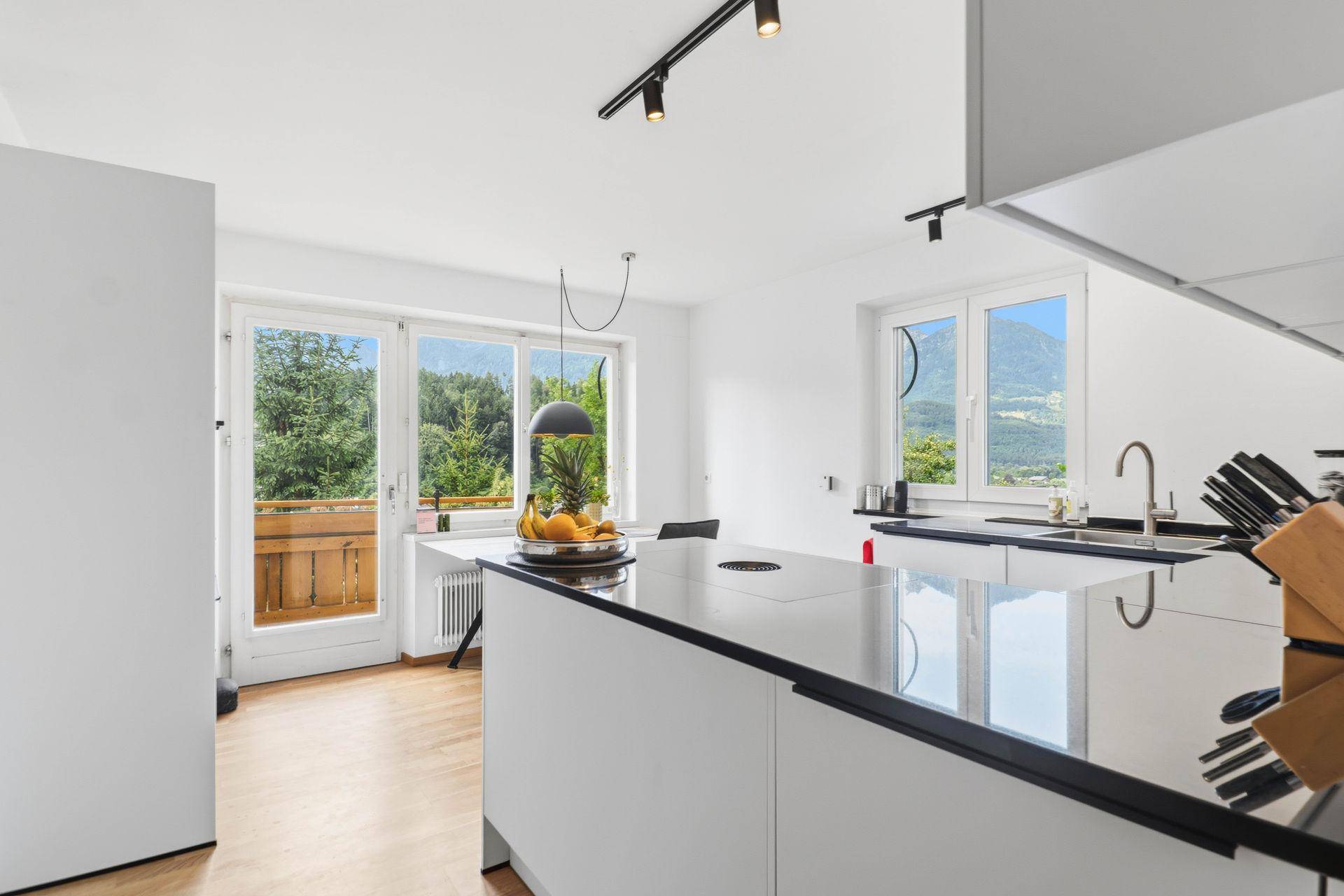 Helle Küche mit Kochinsel, Holzboden und Zugang zu einem Balkon mit Bergblick.