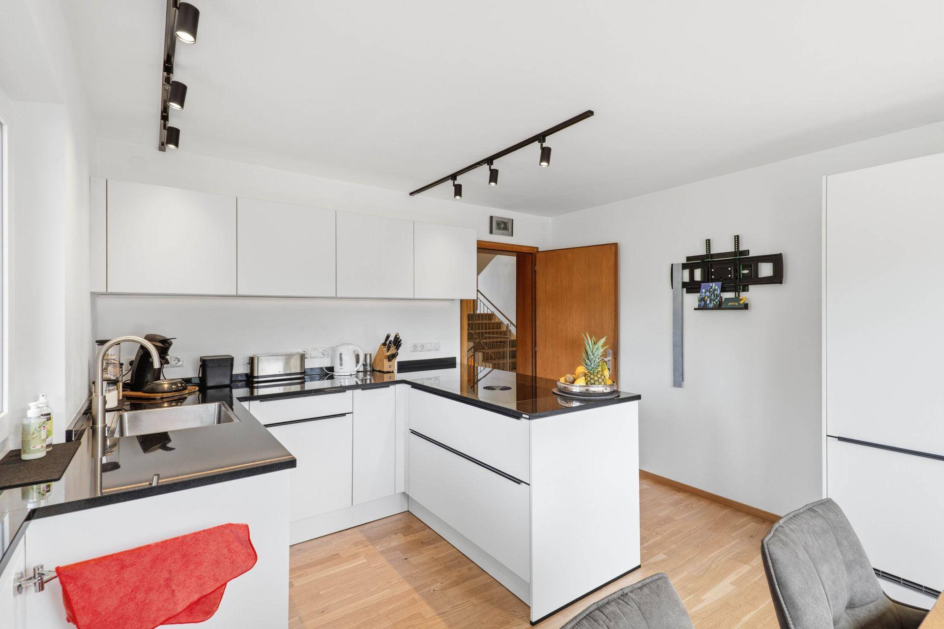 Moderne weiße Küche mit schwarzer Arbeitsplatte, Kochinsel und Holzboden.