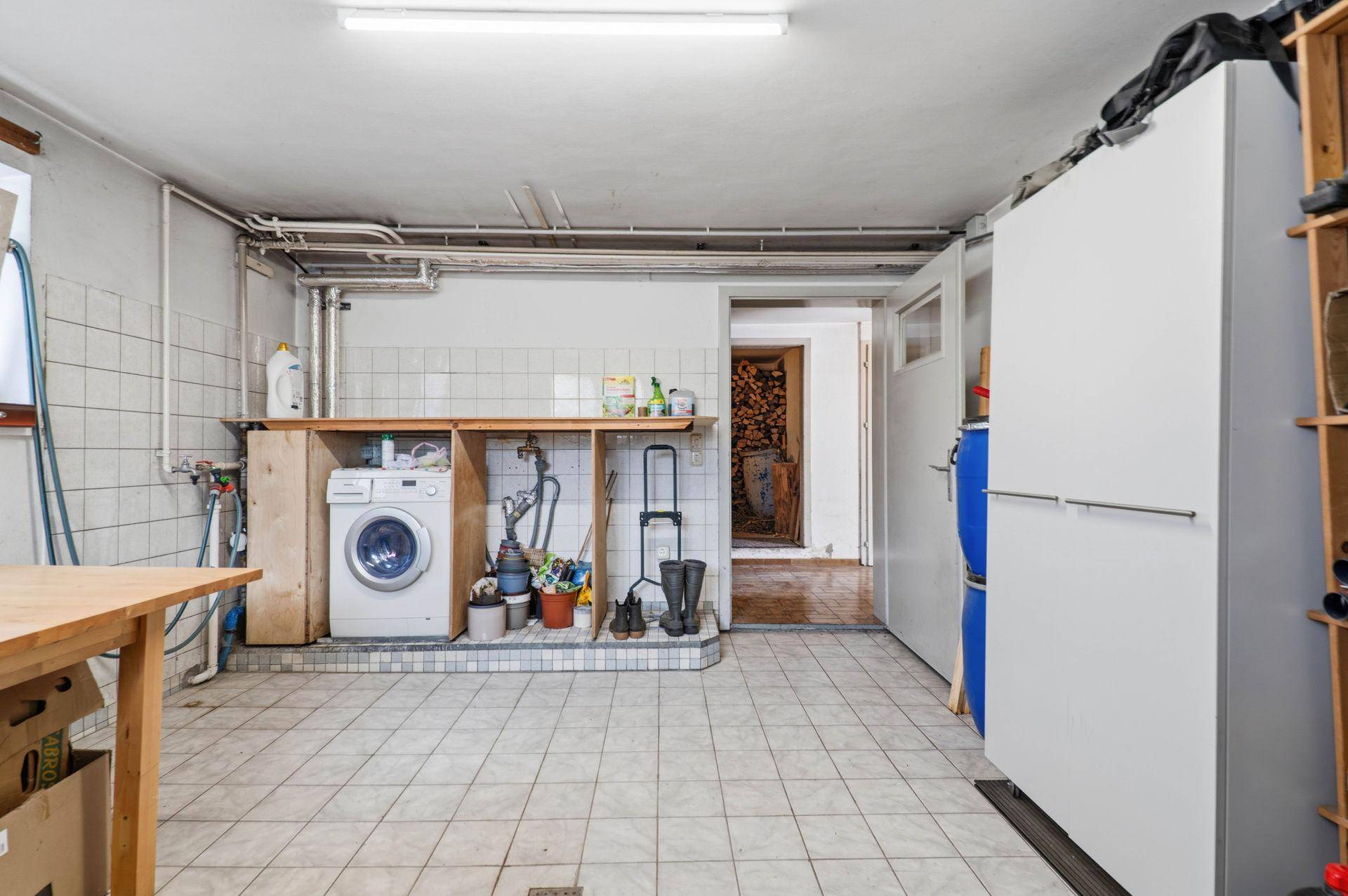 Waschküche im Keller mit Waschmaschine, Spülbecken und Fliesenboden.