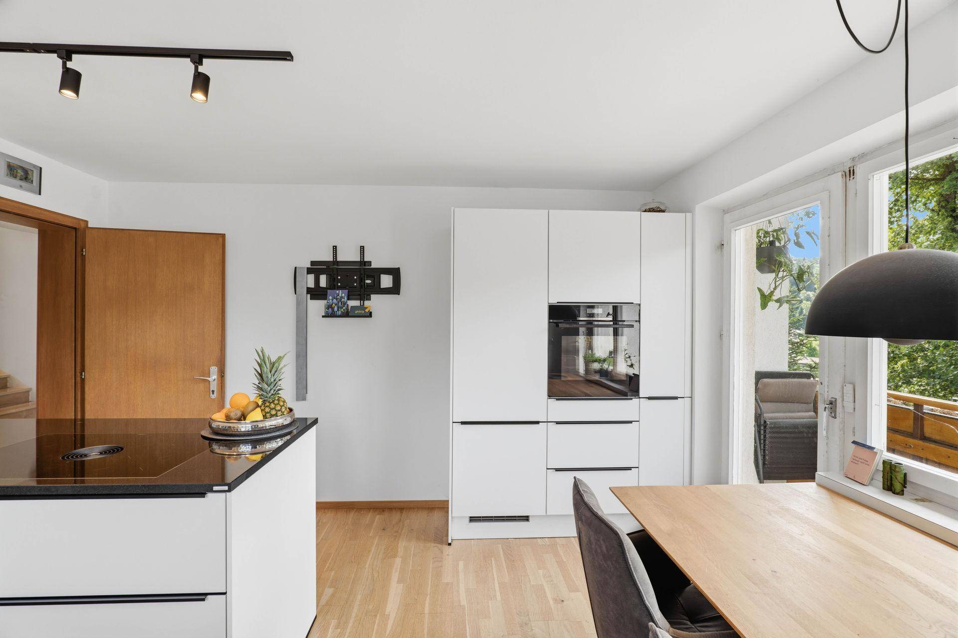 Essbereich in der Küche mit Holztisch, modernen Stühlen und Zugang zum Balkon.