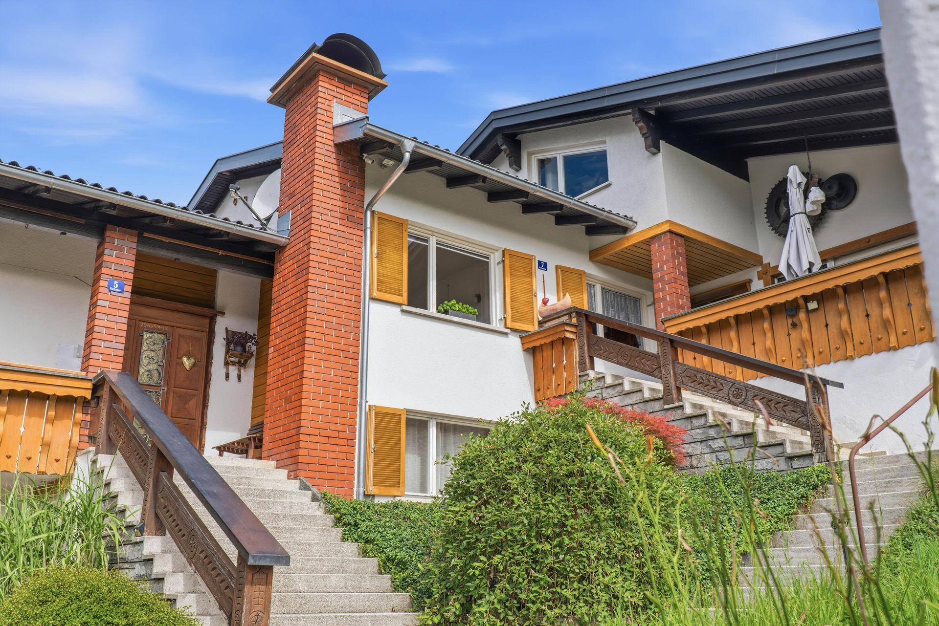 Eingangsbereich eines Hauses mit Steintreppe, Holzgeländer und traditioneller Fassade.