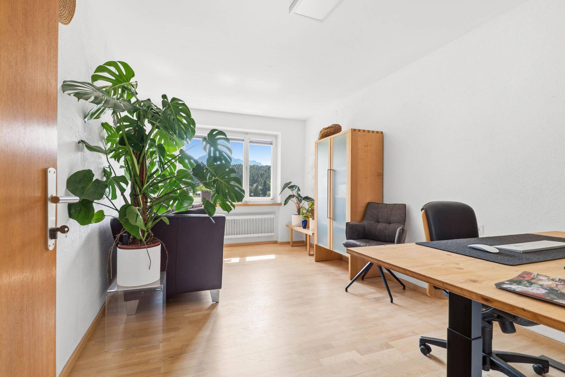 Helles Arbeitszimmer mit Holzboden, Schreibtisch und Blick auf die Berge.